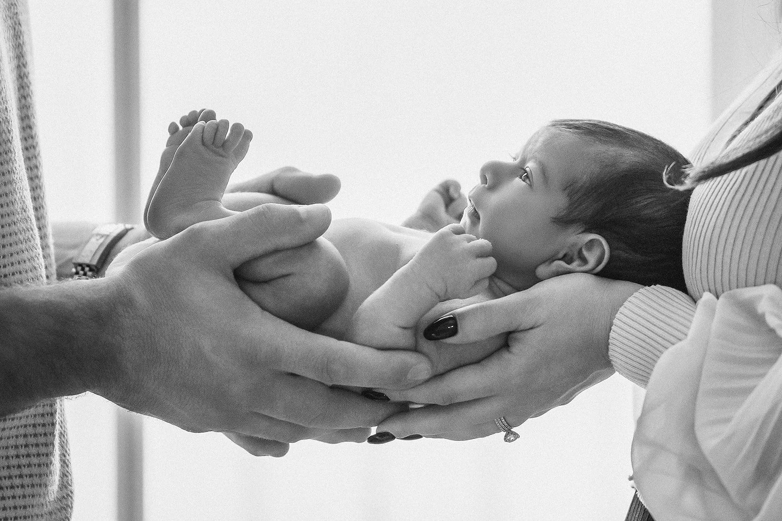 A newborn baby being held by two adults, one supporting the baby's head and the other holding the legs, in a comforting and gentle manner.