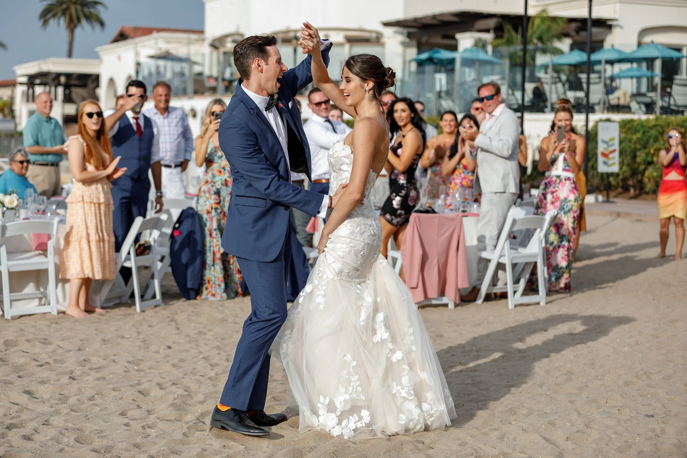 A bride and groom dancing at their beach wedding with guests watching and celebrating in the background.