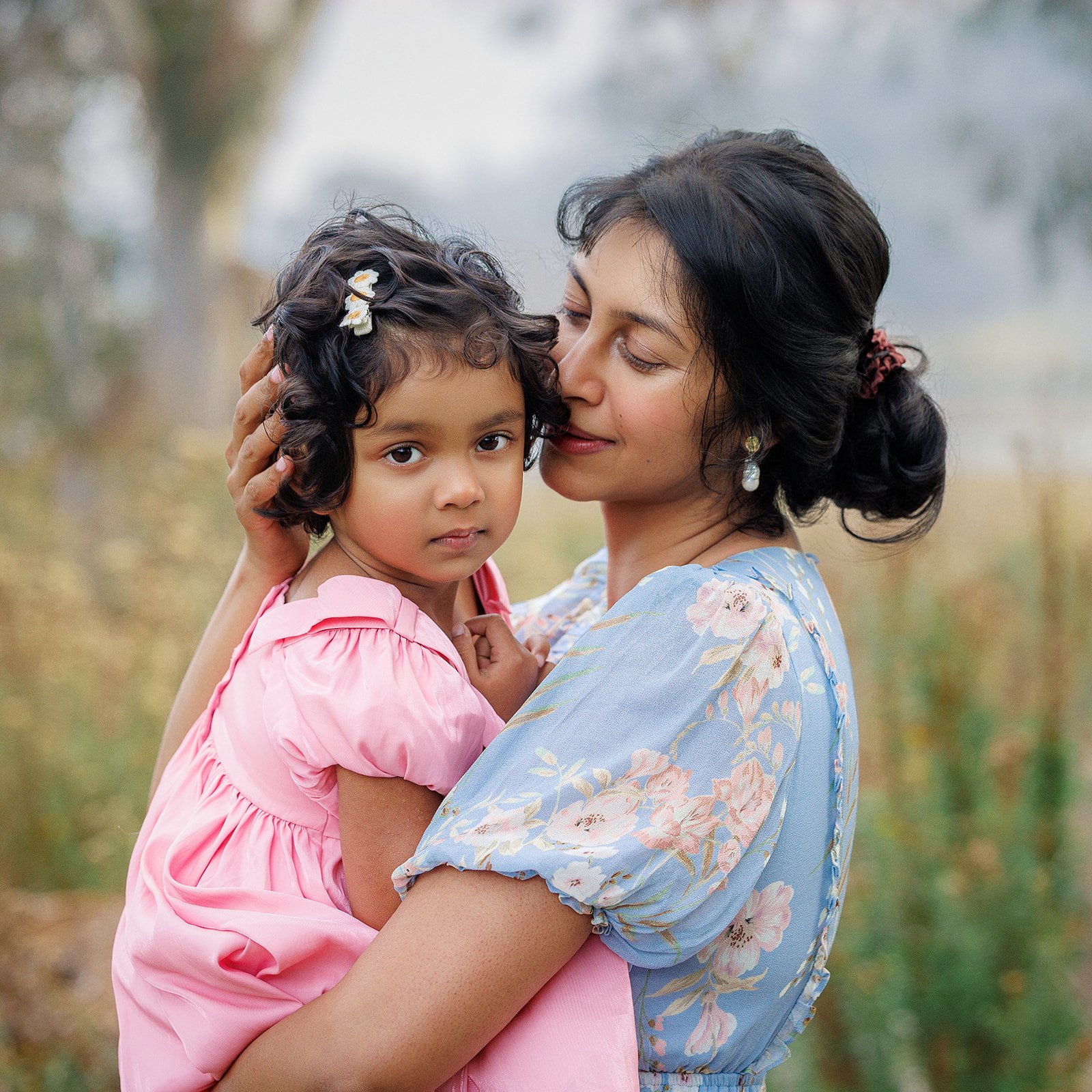 A woman holding a young girl in an outdoor setting with trees in the background.