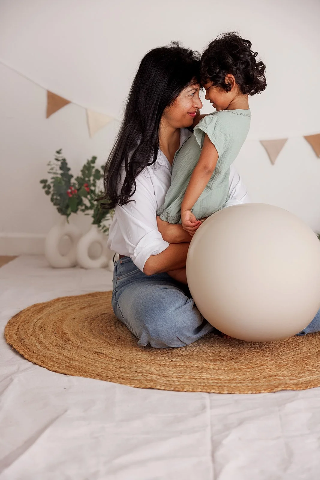 A woman and a young boy playing with a large balloon on a round rug in a decorated room.
