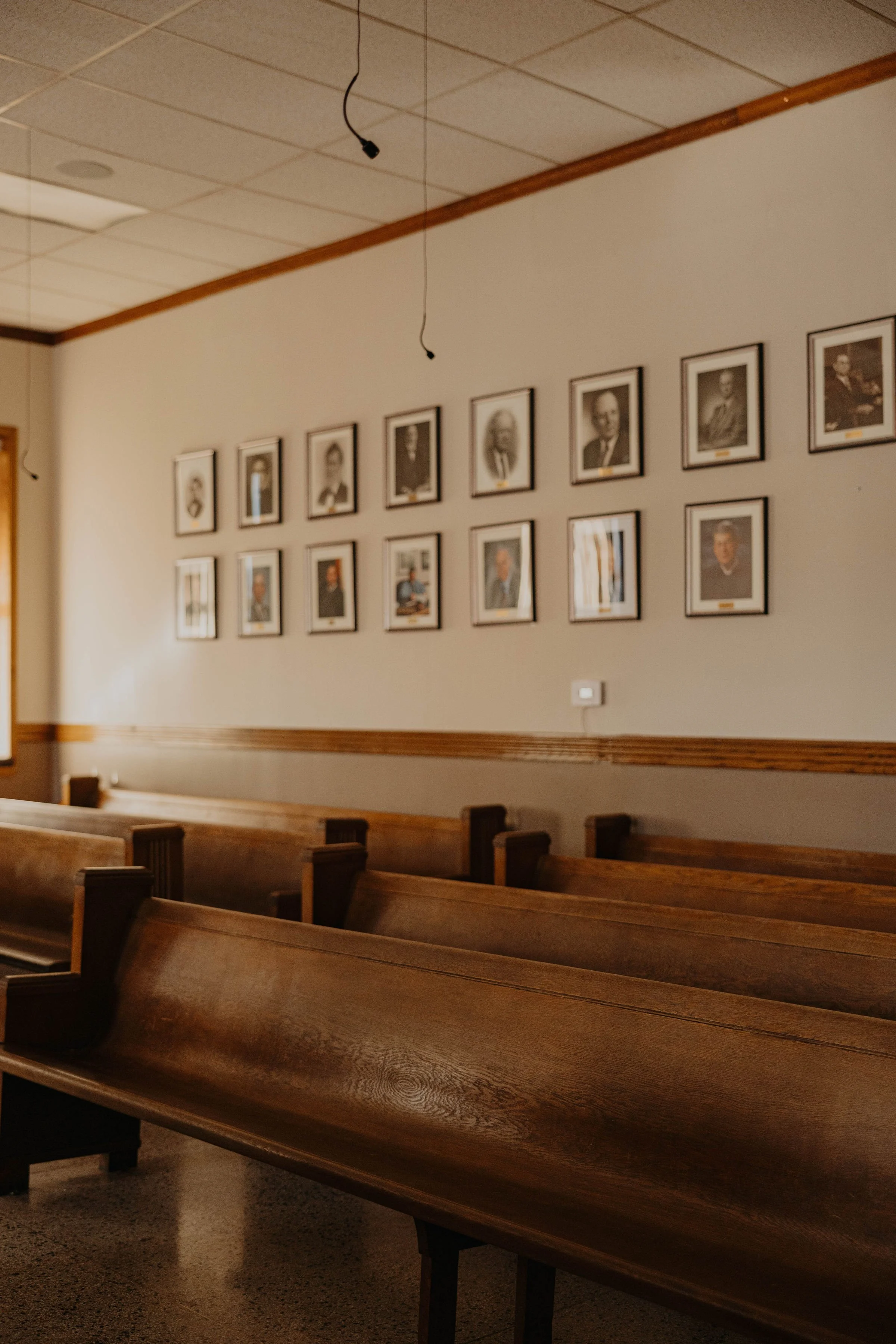 Empty jury/court room pews facing away from a wall with framed portraits of previous judges.