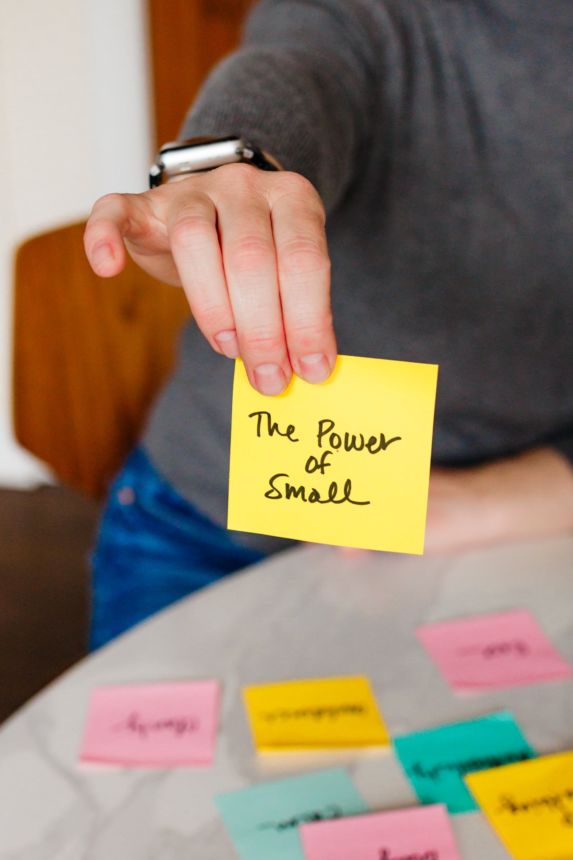 Person holding a yellow sticky note that says "The Power of Small."