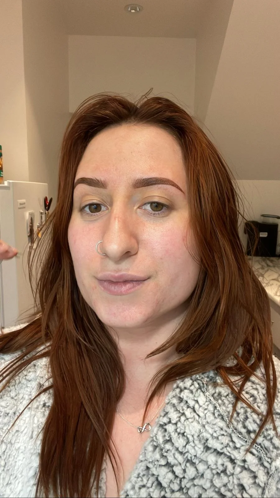 A woman with red hair and a nose ring taking a selfie in a room with a sloped ceiling.