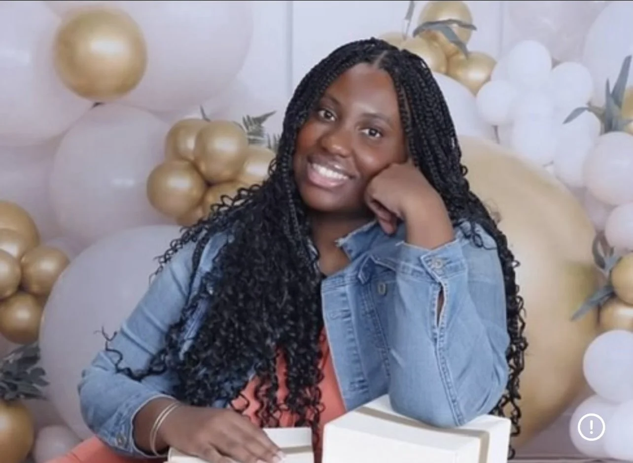 A woman with black hair wearing glasses, a white headband, and a black and white houndstooth patterned jacket, smiling at the camera.