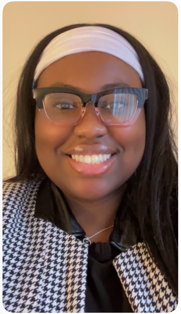 A woman with black hair wearing glasses, a white headband, and a black and white houndstooth patterned jacket, smiling at the camera.