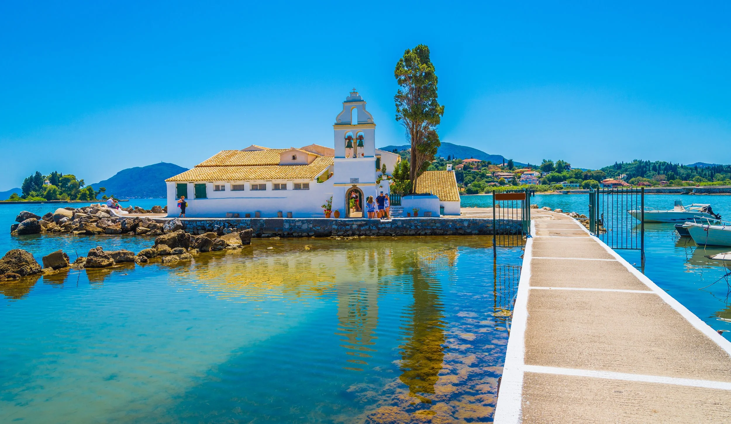 White Vlacherna Monastery on the water in Kanoni, Corfu, with sea views and a footbridge.