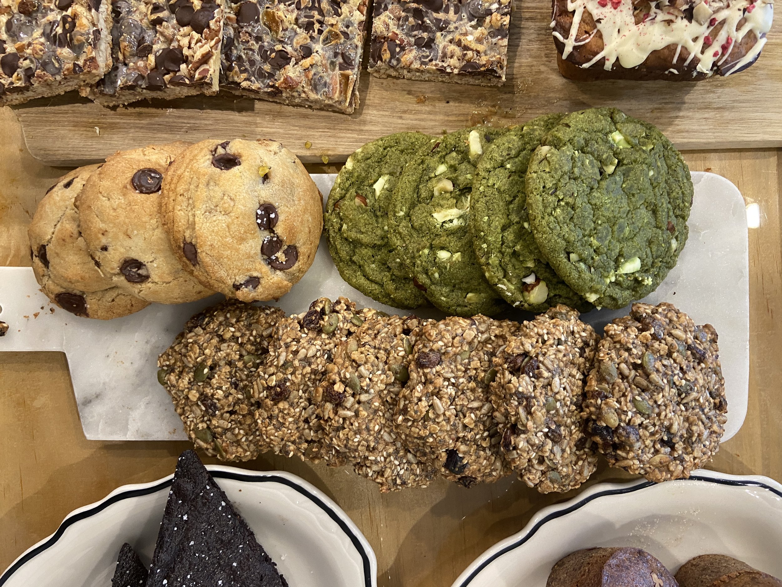 Gâteau, biscuits, cookies aux ingrédients variés, miettes de gâteau aux graines, chocolat noir et autres douceurs sur un plateau en bois.
