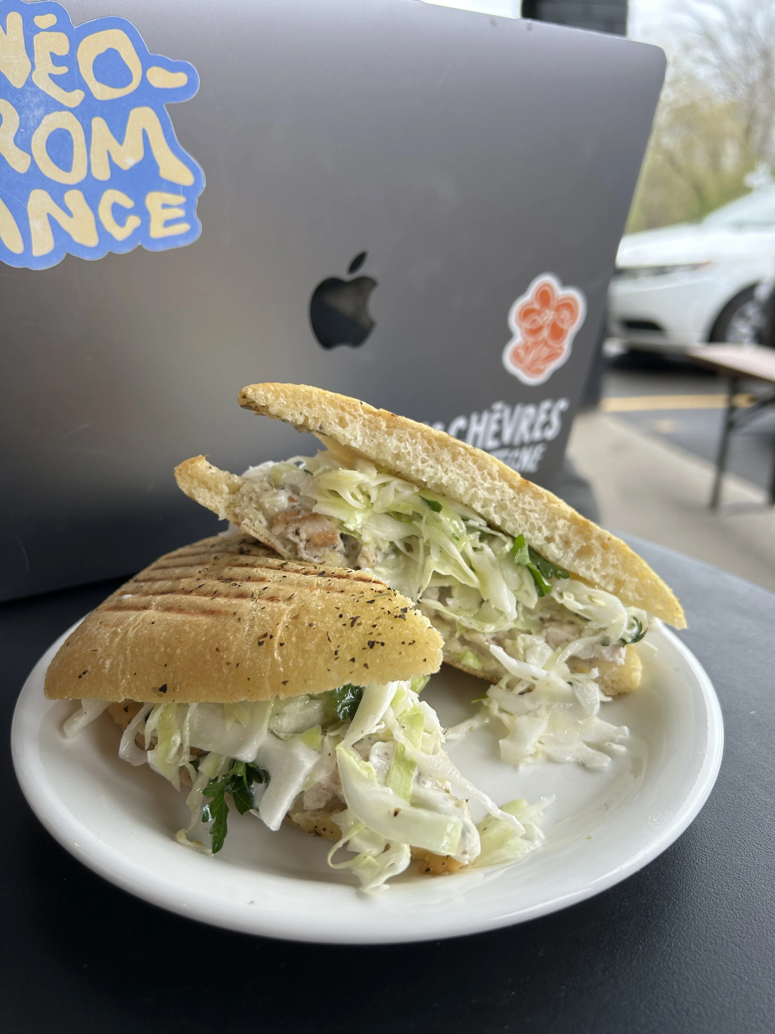 Sandwich au poulet avec salade dans un pain baguette, placé sur une assiette blanche, avec un ordinateur portable en arrière-plan.