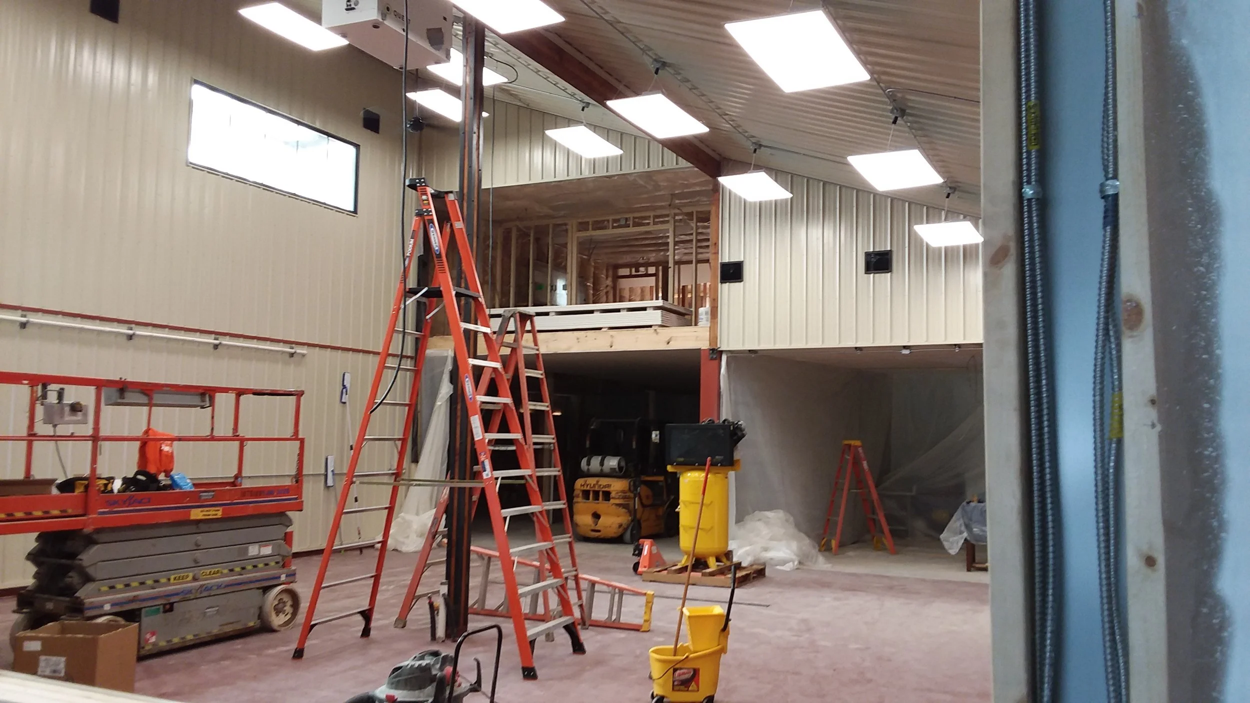 Interior of building under construction with vaulted ceiling and an assortment of ladders and equipment.