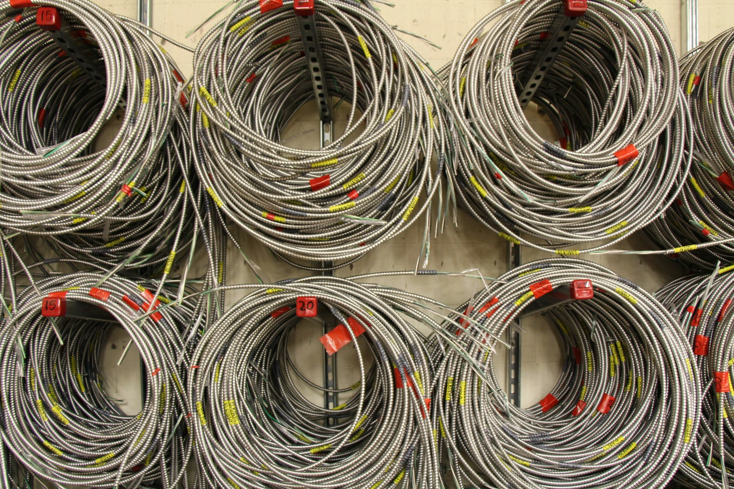 Coiled metallic cables hanging on hooks in a storage area with numbered tags.