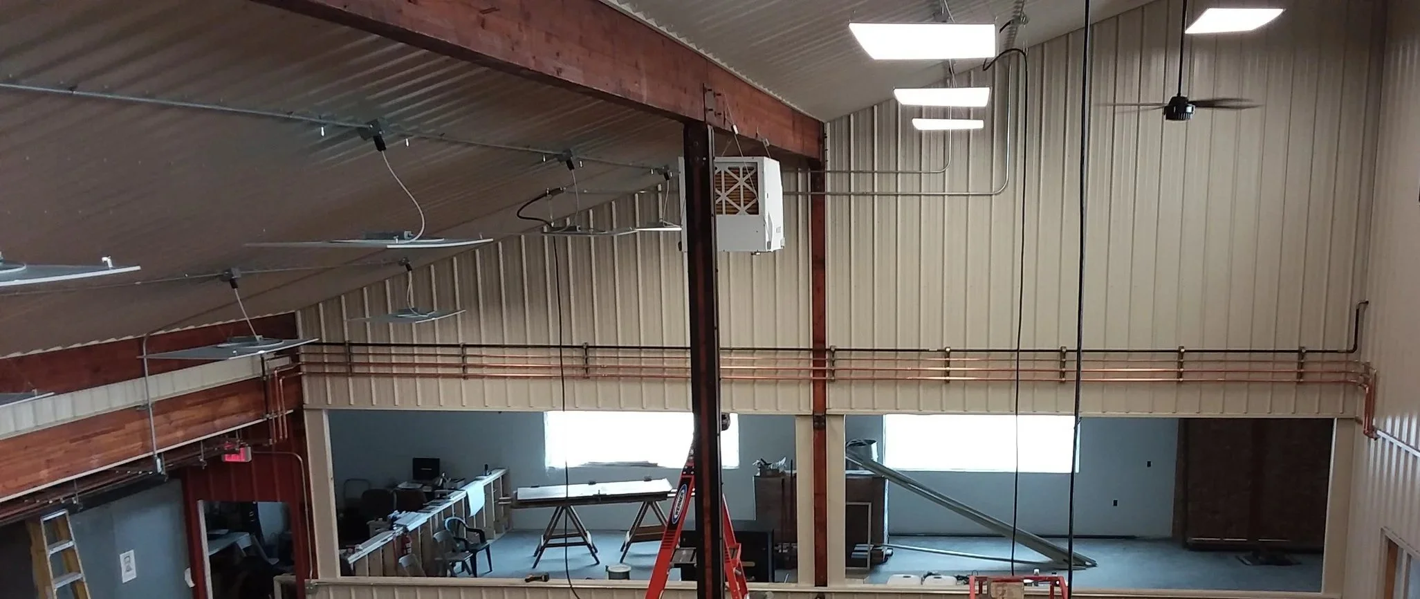 Interior of building under construction showing a large ceiling beam, suspended lights, and ceiling fans.