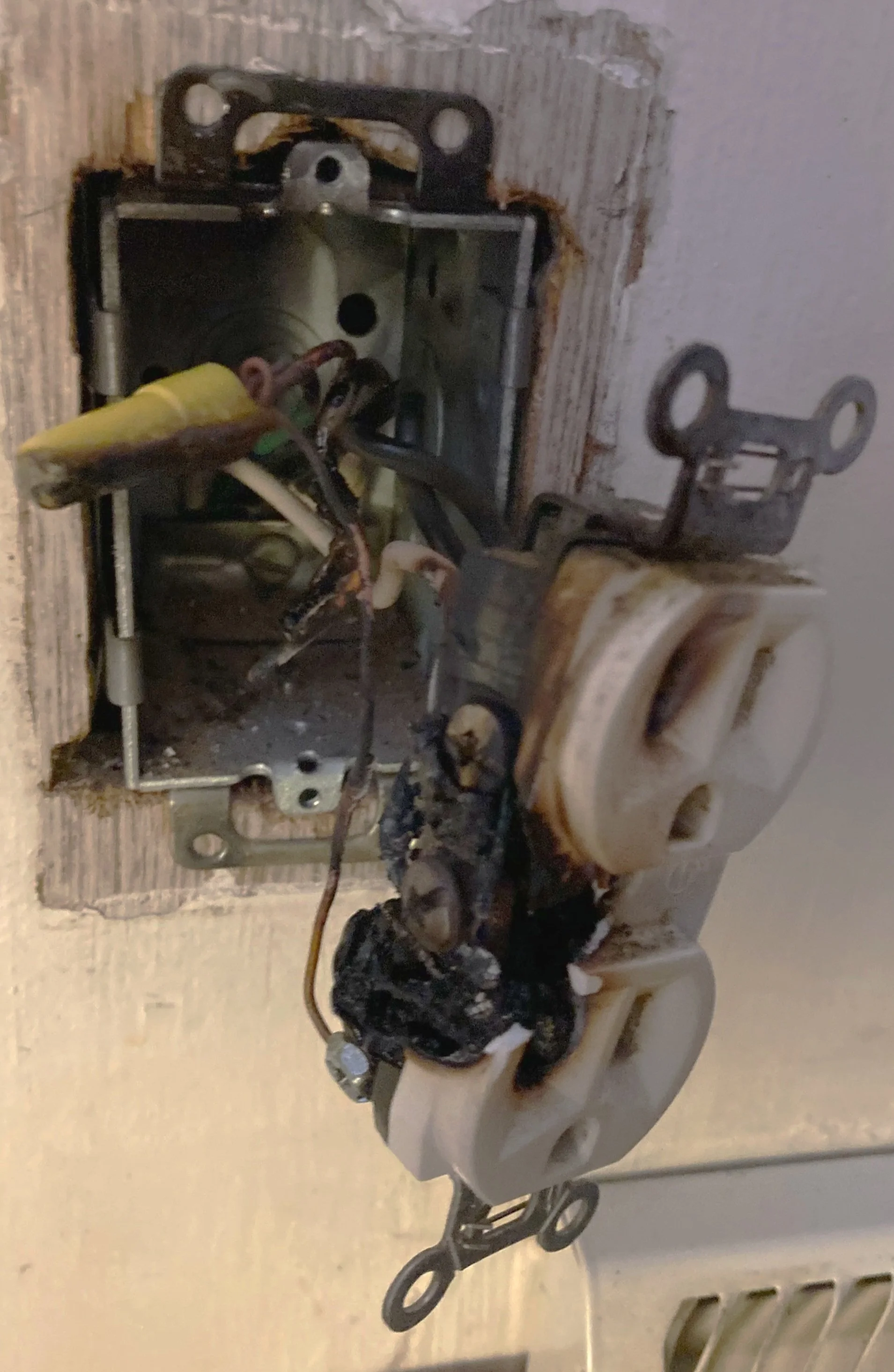 A burnt and blackened wall receptacle partially pulled out of the wall.