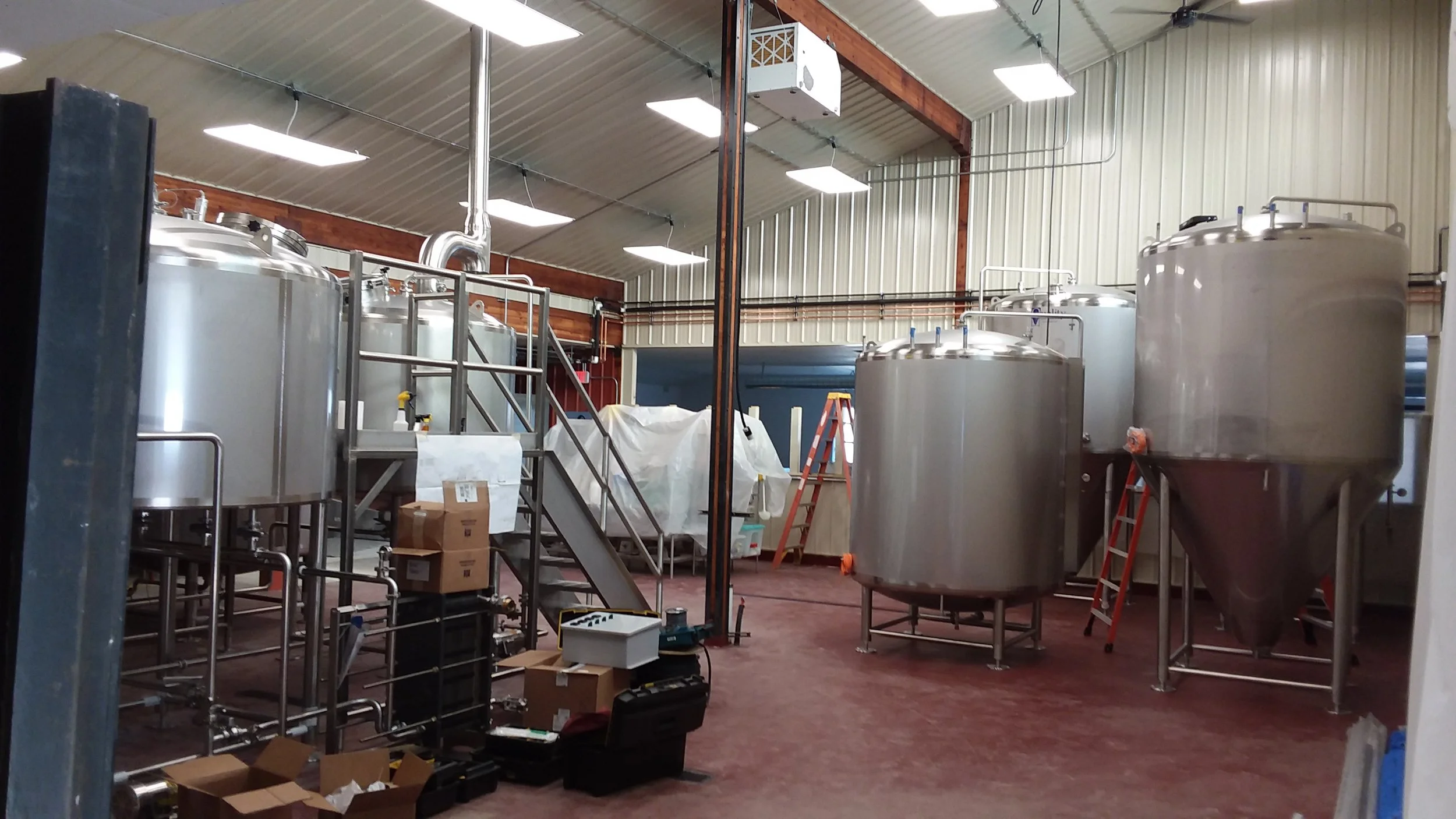 Large vaulted interior space with red floor and multiple stainless steel brewing tanks.