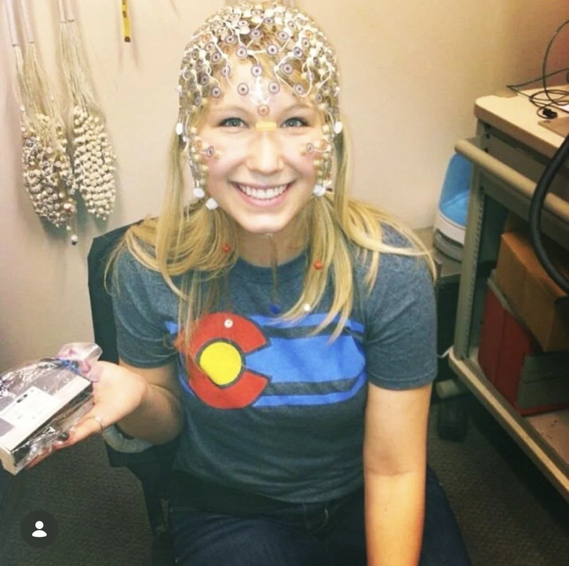 Author and Founder Sammy sits smiles for a photo wearing a EEG (electroencephalogram) net during her time at the University of Oregon's Child and Family Center's brain and behavior lab.