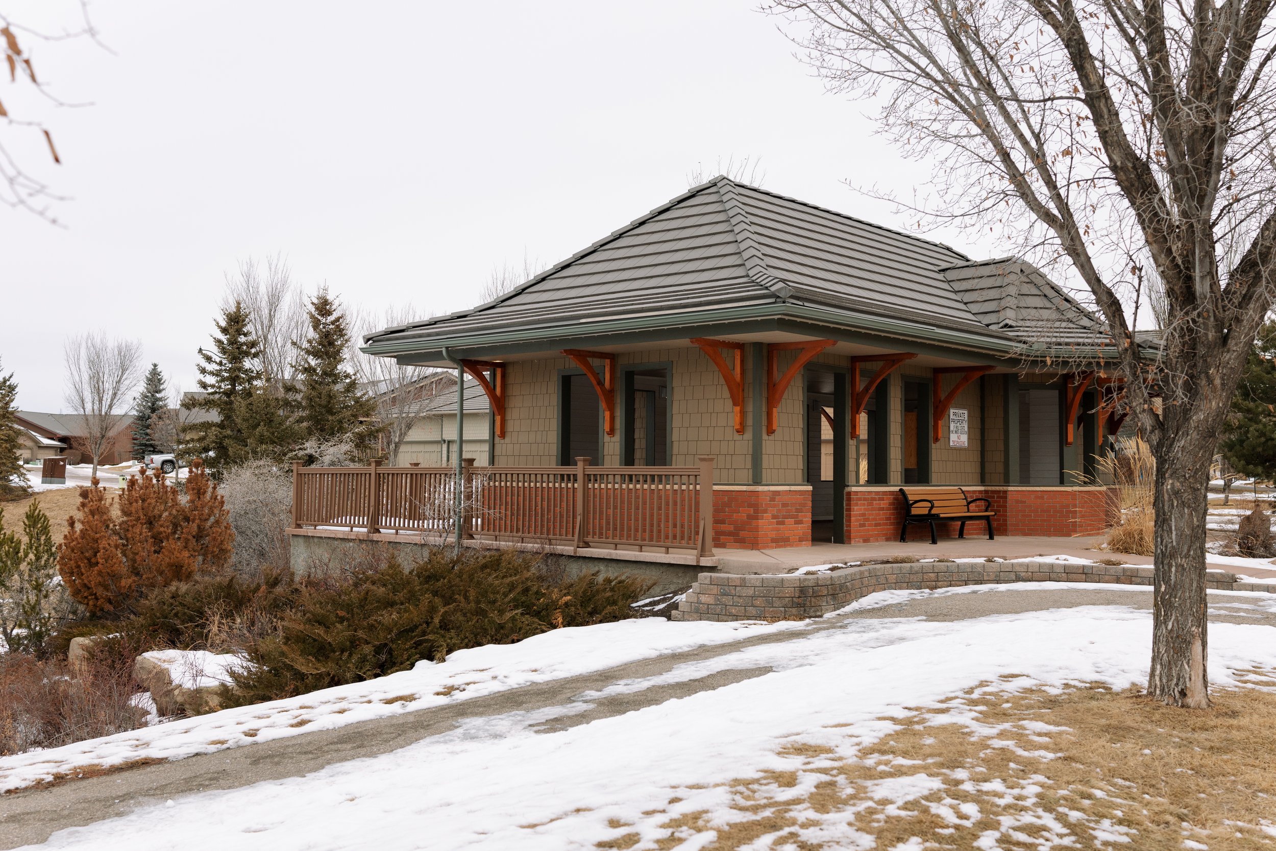 A single-story house with a covered porch, brick and siding exterior, surrounded by leafless trees and some snow on the ground.