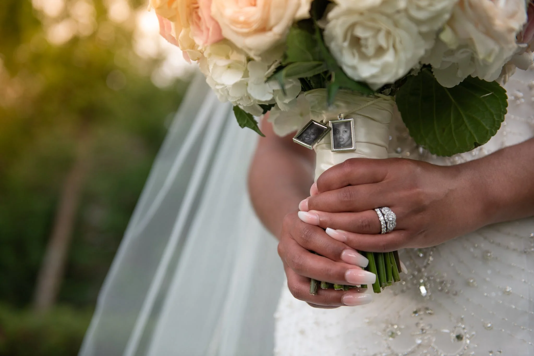 Close-up of a bride holding a wedding bouquet with earrings hanging from the bouquet, showing her wedding ring and manicured nails.
