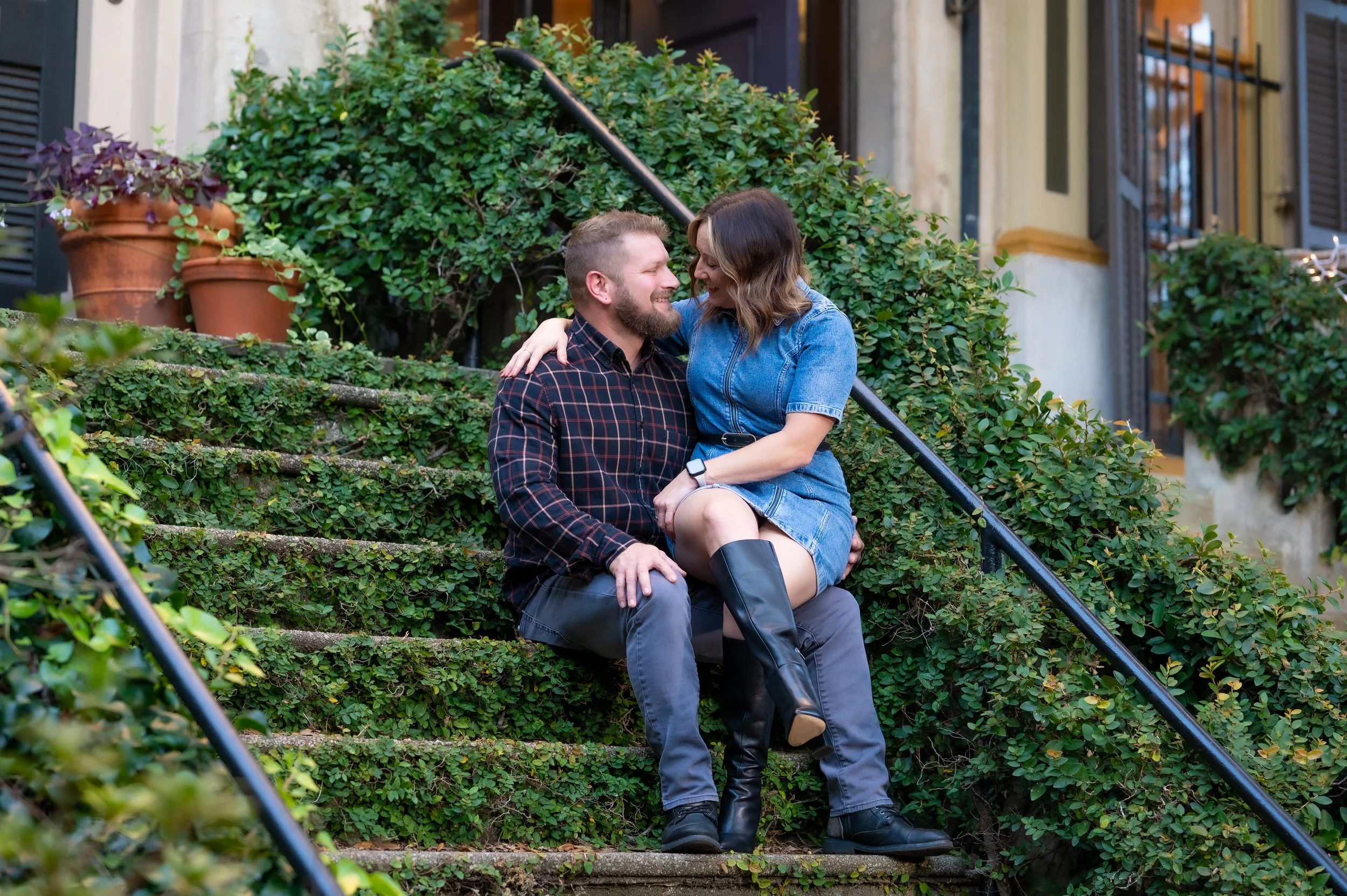 A couple sitting on outdoor steps surrounded by greenery, smiling and looking into each other's eyes.