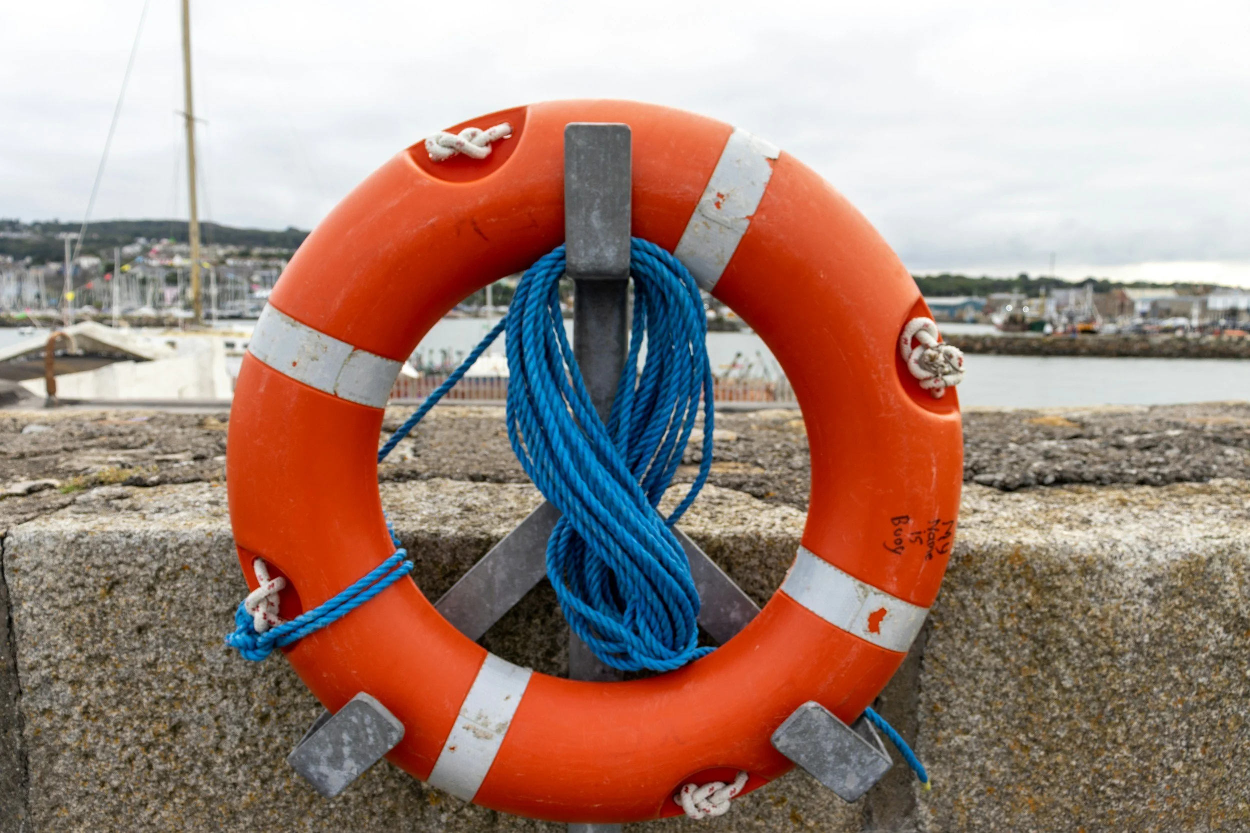 A life buoy with a blue rope attached, placed on a concrete surface near a marina or harbor