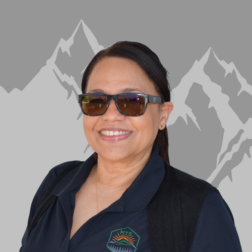 A woman wearing sunglasses and a dark polo shirt with an embroidered logo, smiling, with a backdrop of stylized mountain peaks.