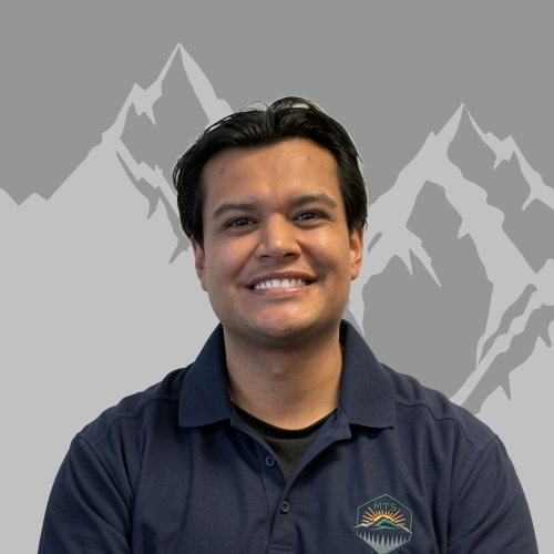 A young man smiling at the camera, wearing a navy polo shirt with a mountain logo on it, standing in front of a background featuring stylized gray mountains.