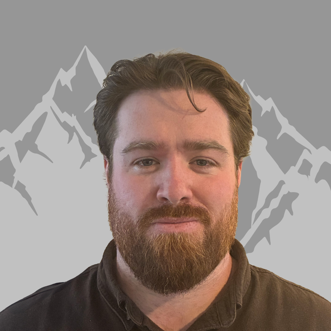 A man with a beard and dark hair against a mountain silhouette background.