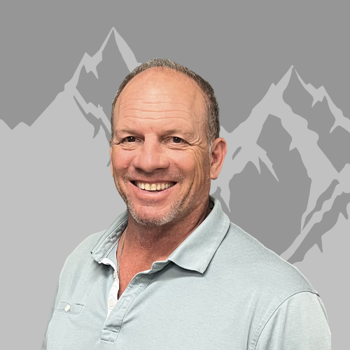 smiling middle-aged man with short hair and stubble, wearing a light gray polo shirt, against a backdrop of stylized gray mountain peaks.