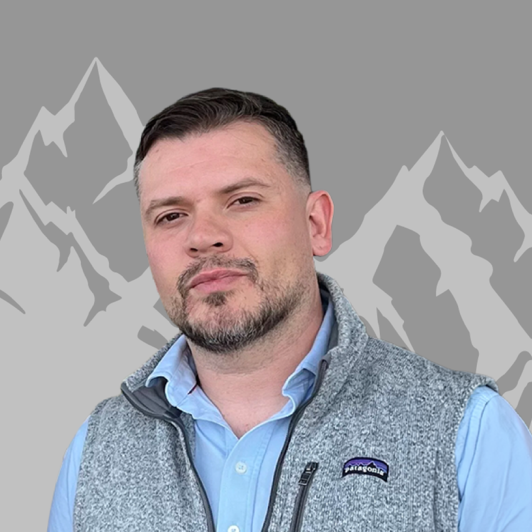 Portrait of a man with short dark hair and light beard, wearing a blue shirt and gray Patagonia vest, standing in front of a stylized mountain backdrop.