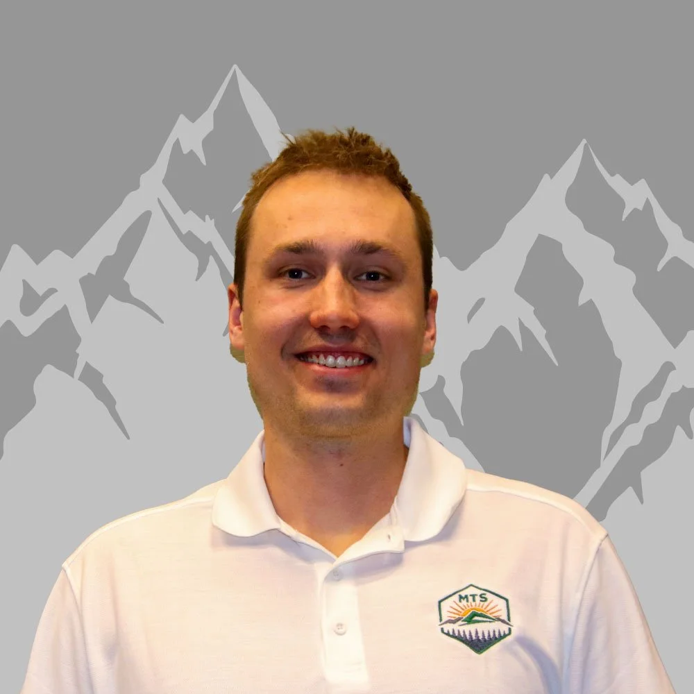 A smiling man with short brown hair wearing a white polo shirt with a mountain and sun logo, standing in front of a stylized mountain background.