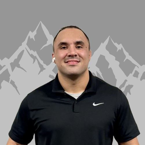 A man smiling, wearing a black Nike polo shirt, standing in front of a digital background with mountain illustrations.