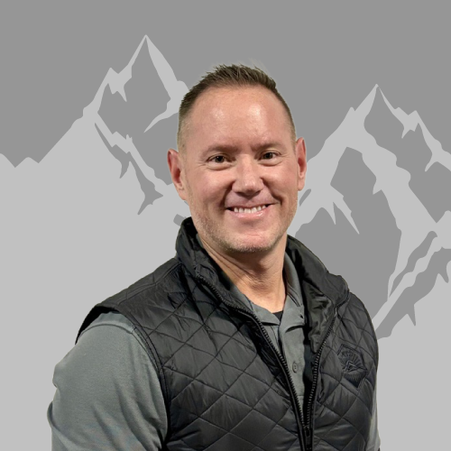 Smiling man in a gray shirt and black vest standing in front of a mountain graphic background.