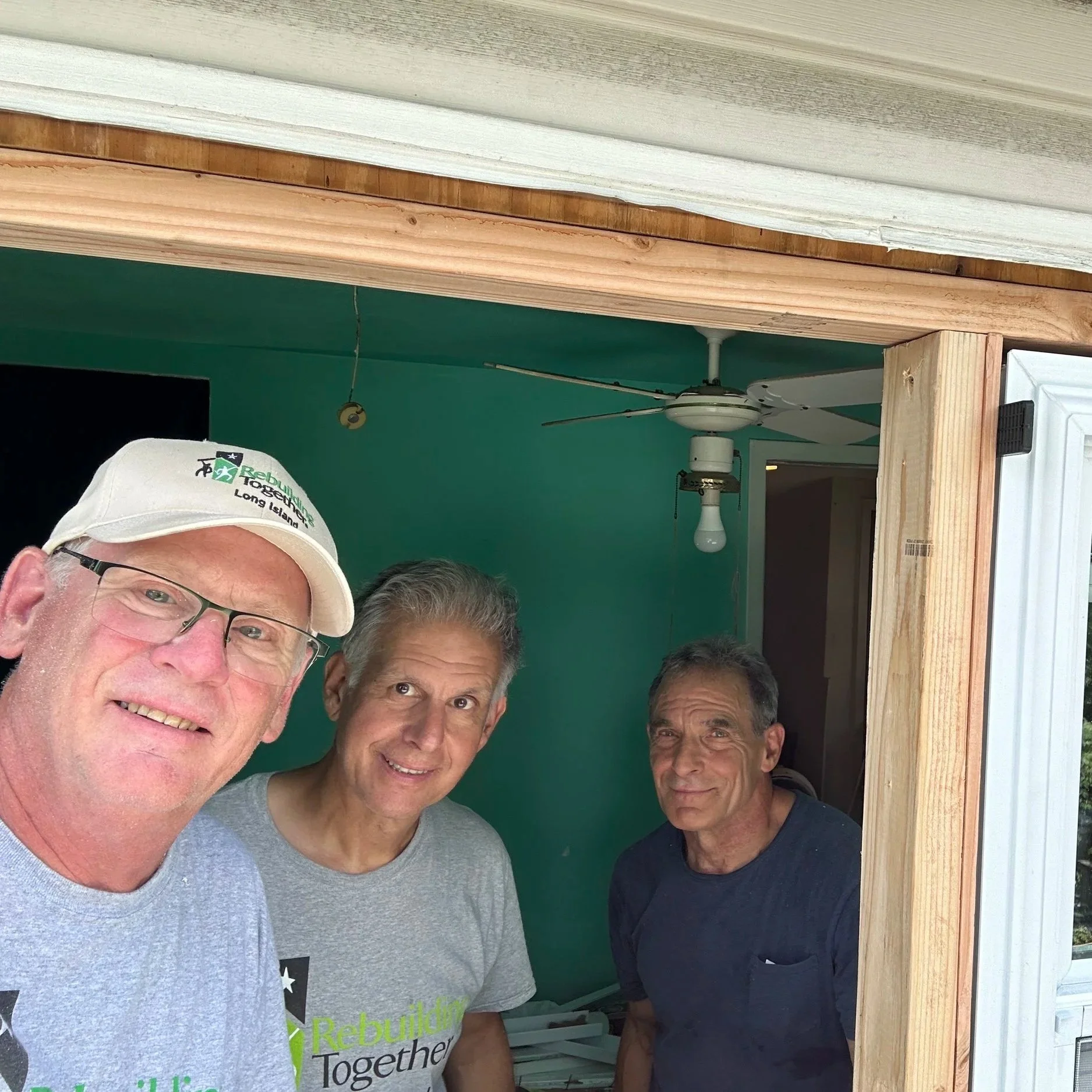 Three smiling male volunteers in tee shirts in doorway of room of job site