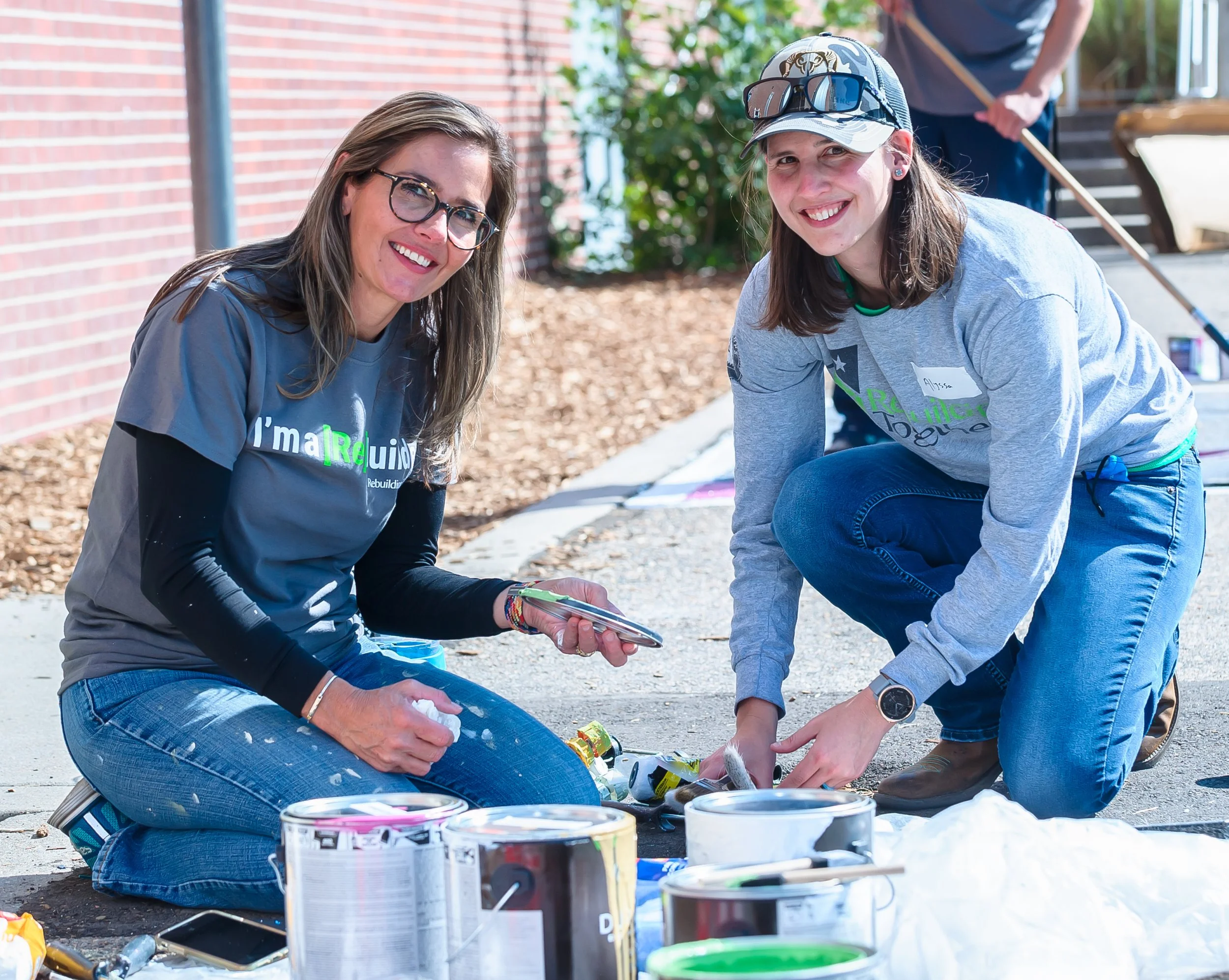 Two femaile volunteers in gray shirts mixing paint and smiling