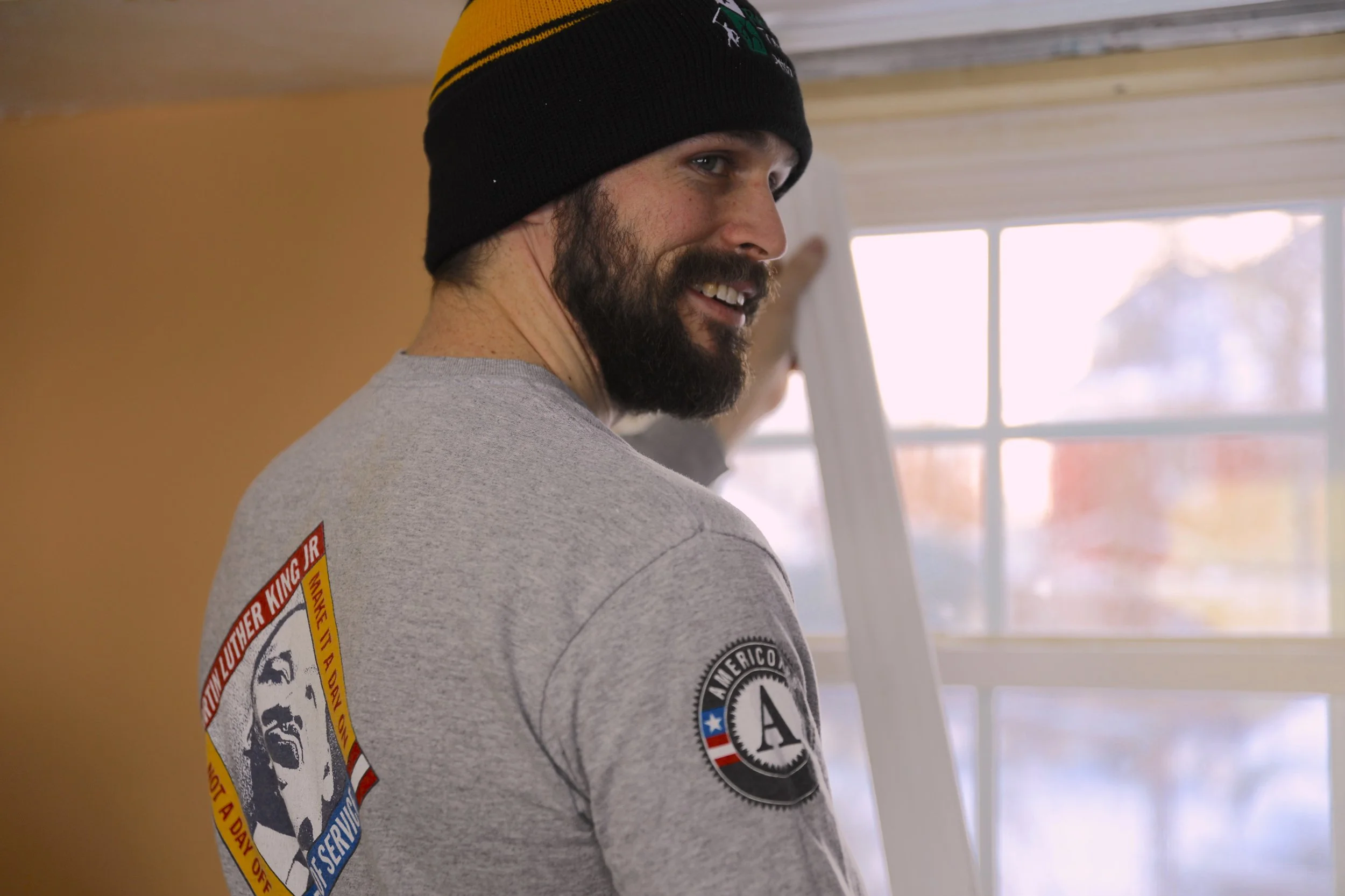 Male smiling volunteer in gray shirt and black hat looking over his shoulder
