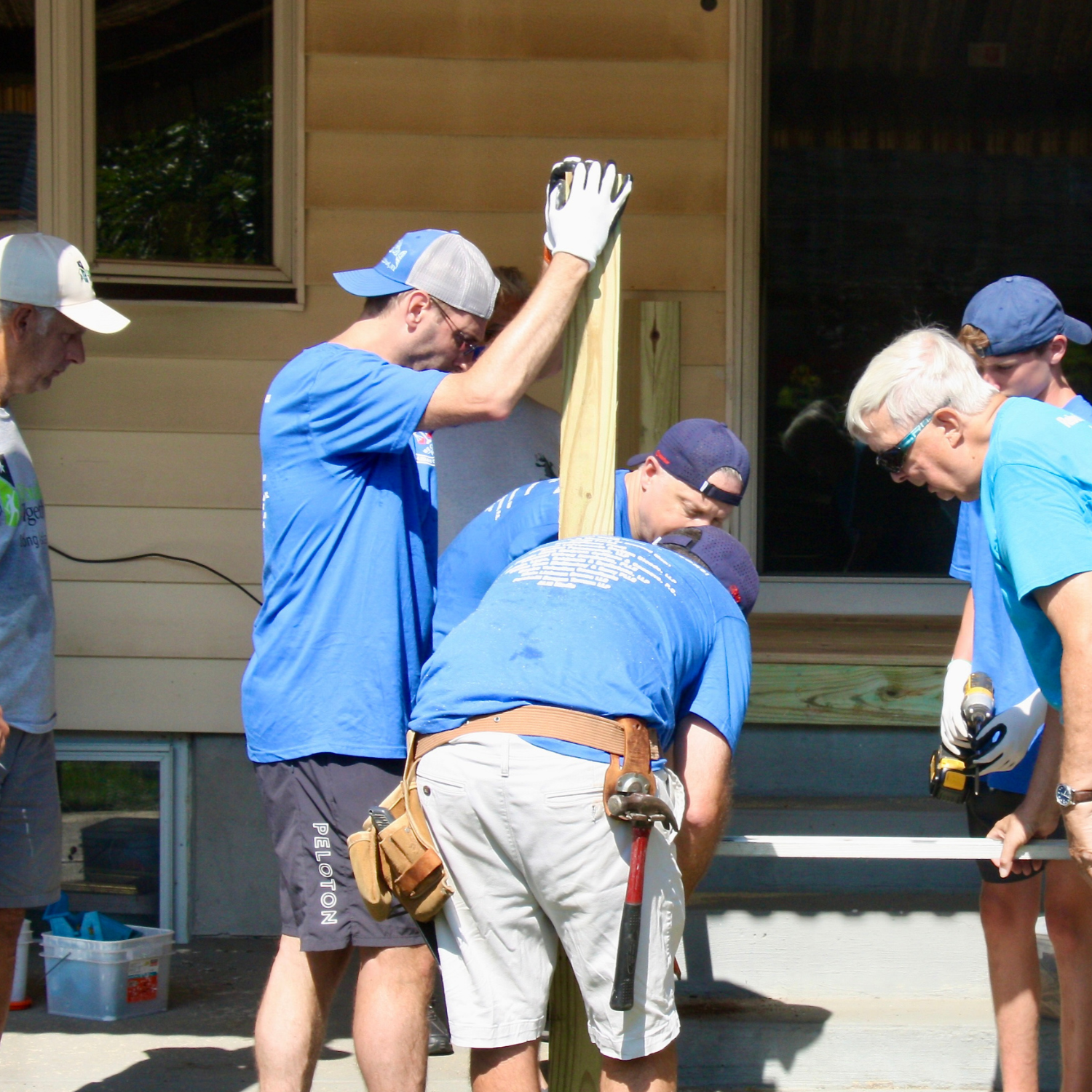 Six male volunteers in blue tee shirts installing a post for an outdoor ramp