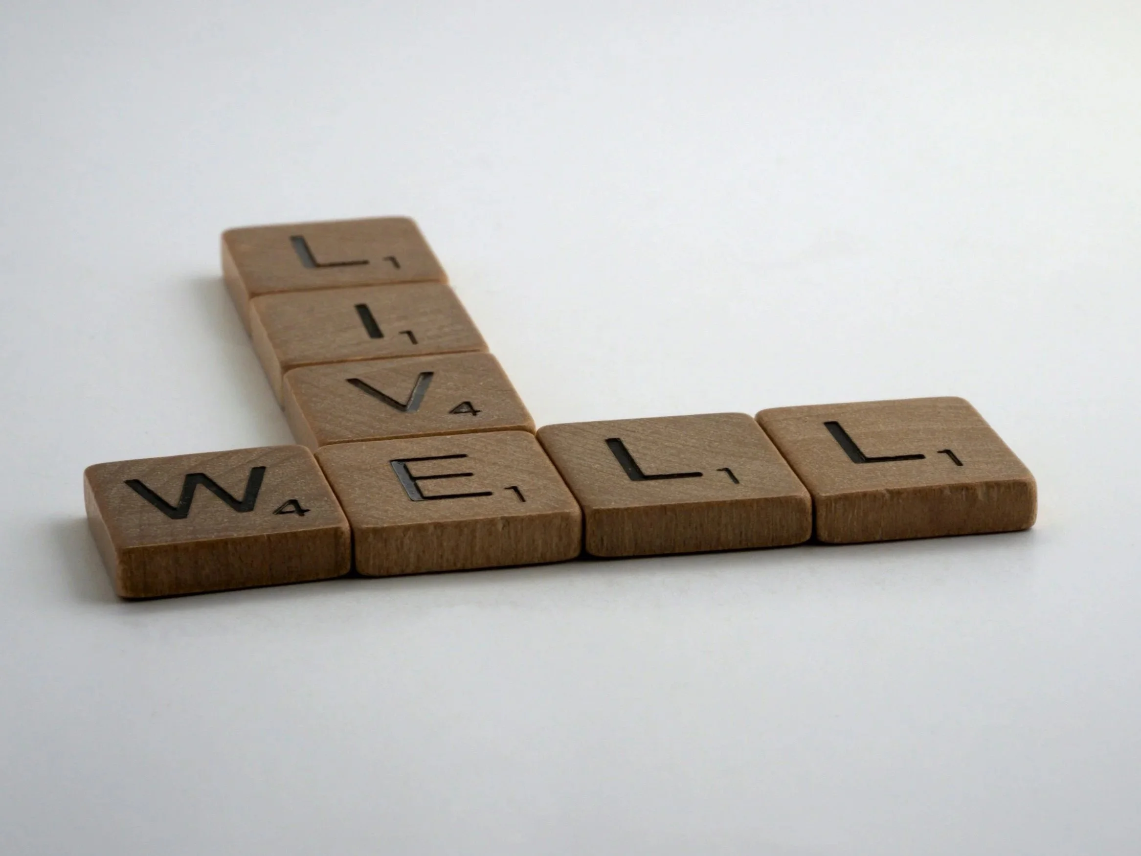 Wooden Scrabble tiles spelling the words "LIVE" 'WELL' on a white surface. Holistic Healing acupressure in Easton, MD leads to better living