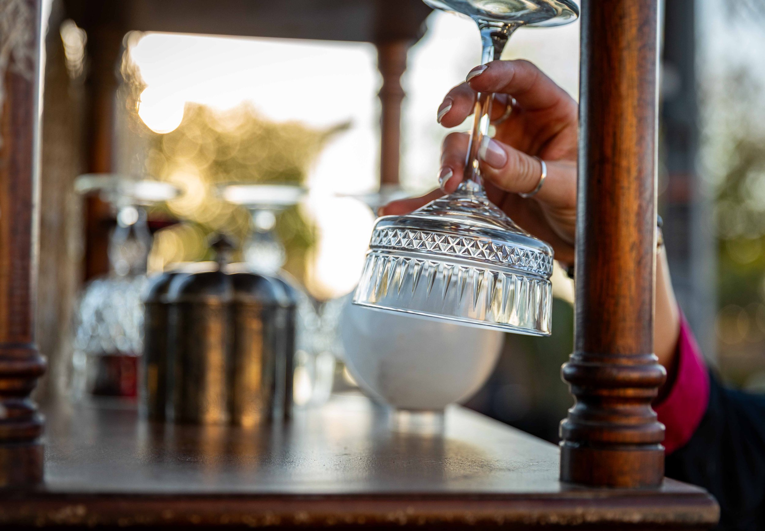 Person holding an upside-down glass on a wooden bar with other glasses and blurred background.