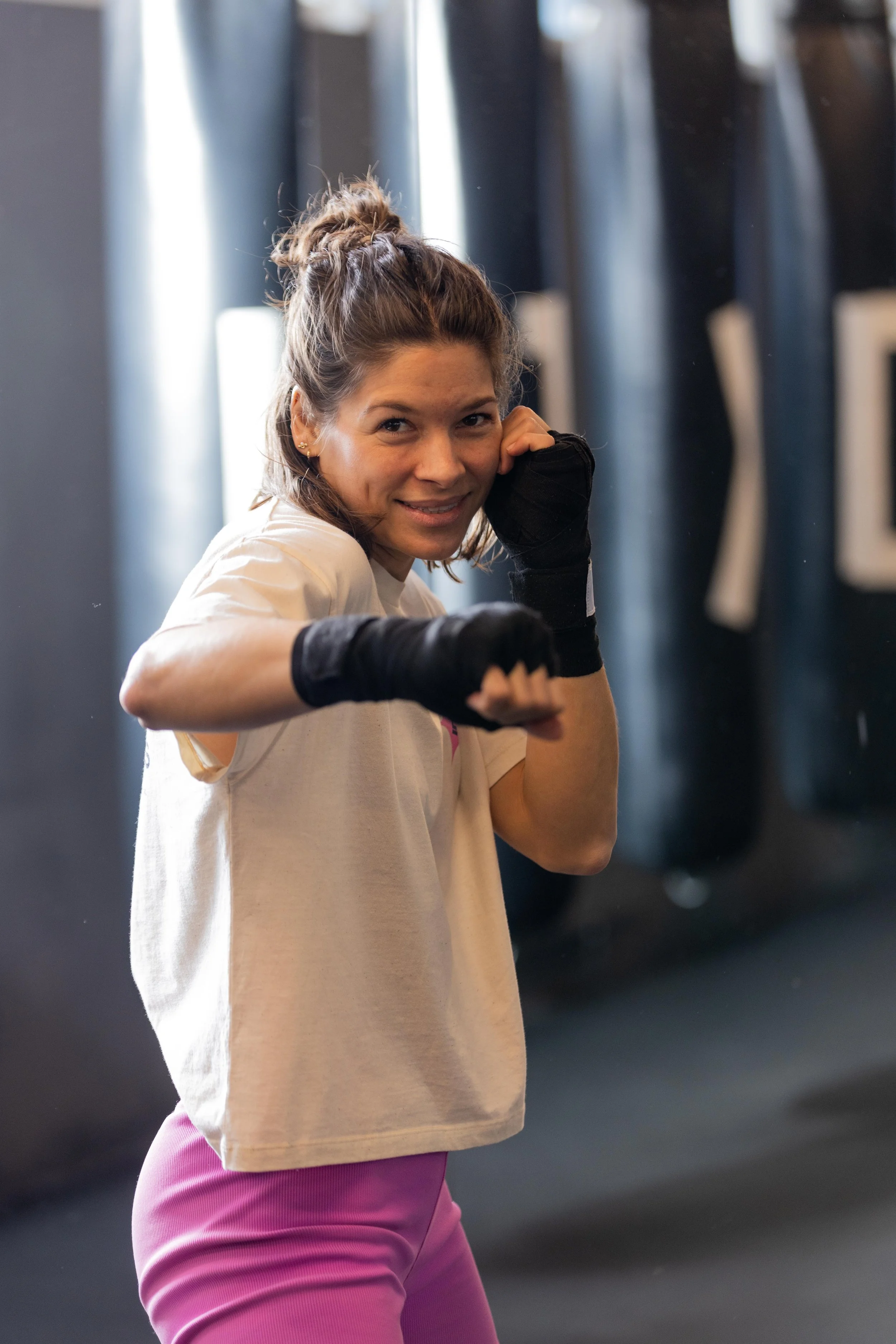 Frau in einem Fitnessstudio in Frankfurt am Main, die eine Boxer- oder Kampfsporttechnik übt, mit schwarzen Boxhandschuhen, lächelnd in die Kamera blickend.