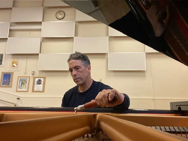 Registered piano technician servicing a grand piano in San Francisco, demonstrating professional piano tuning and maintenance inside a music studio.