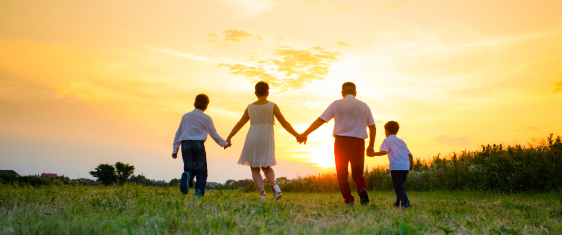 Family holding hands and walking in a field at sunset.