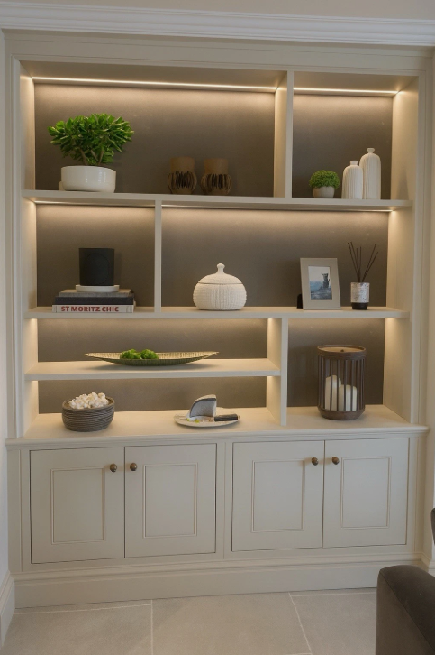 Decorative built-in white shelving unit with various plants, vases, books, and picture frames, illuminated with warm LED lighting.