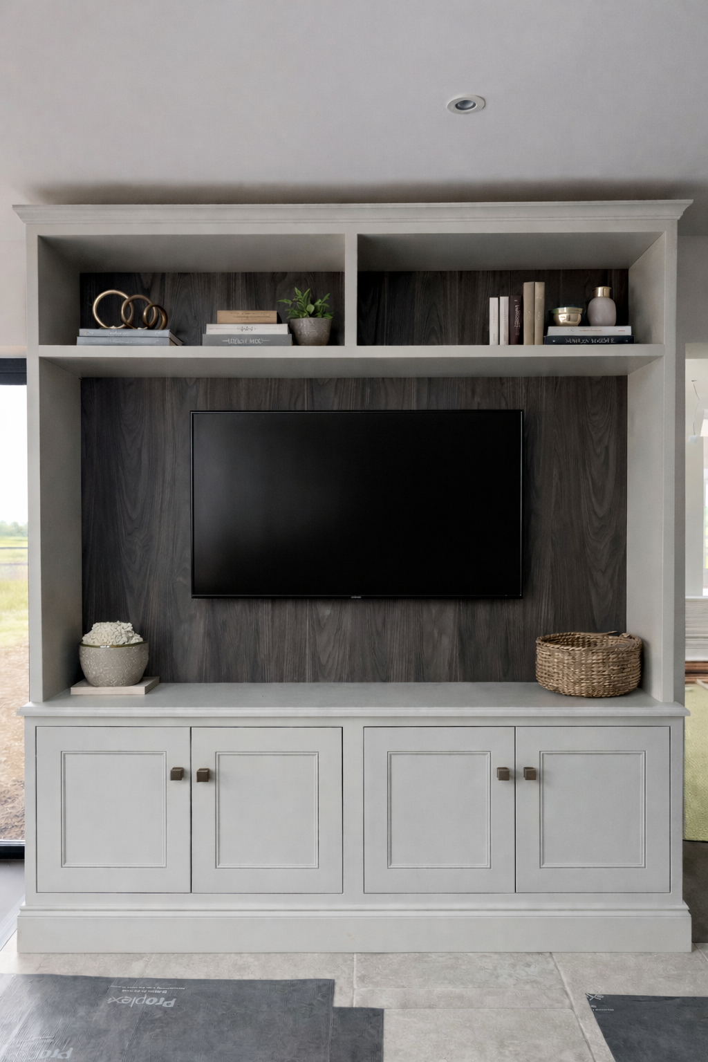Living room media console with shelves, a flat-screen TV, decorative items, books, and a potted plant.