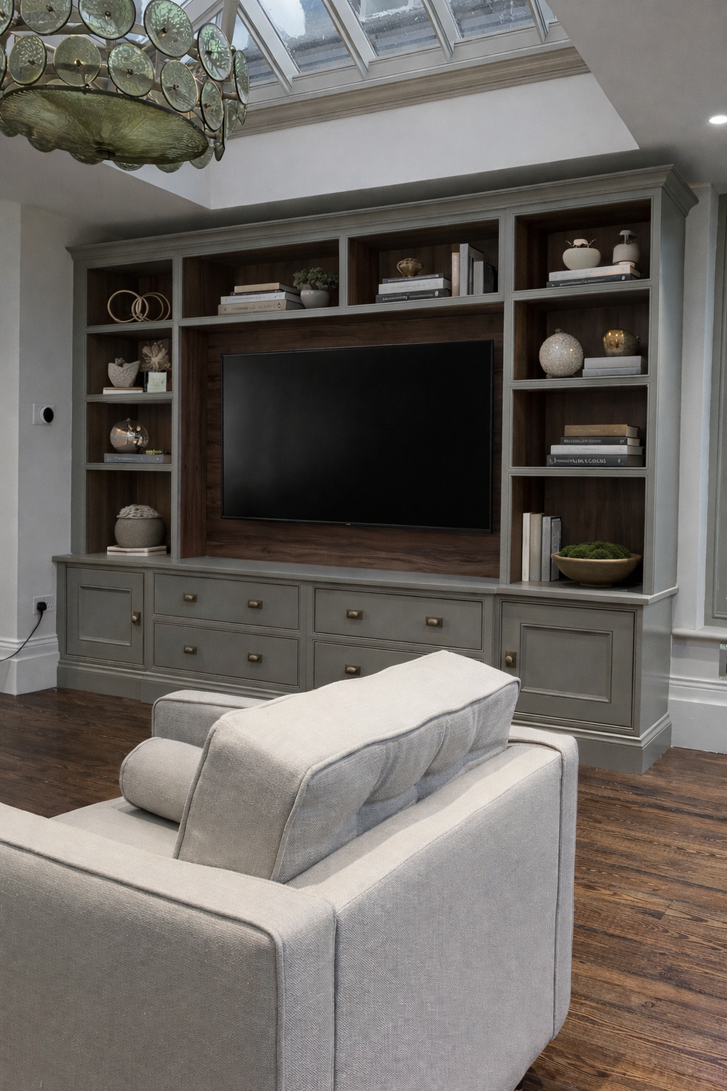 Living room with a built-in entertainment center, a wall-mounted TV, and a beige sofa, in a room with wood flooring and a glass ceiling.