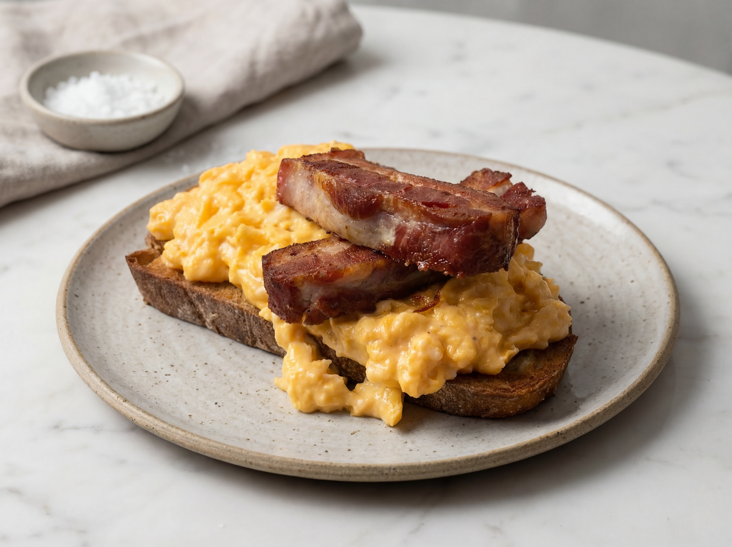 A plate with scrambled eggs and crispy bacon on toasted bread