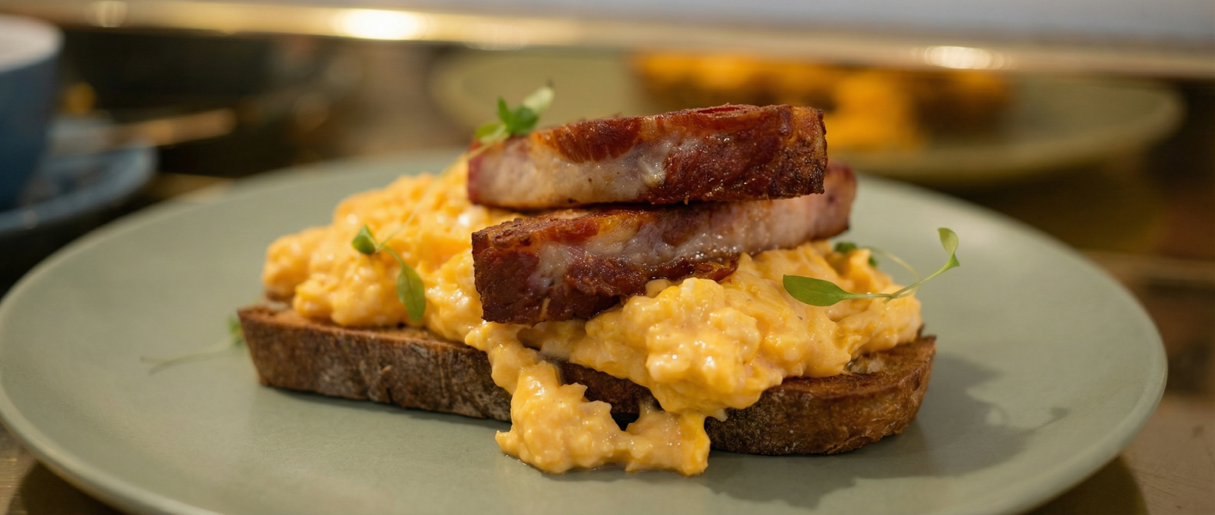 Scrambled eggs on toast topped with crispy bacon garnished with small green leaves.