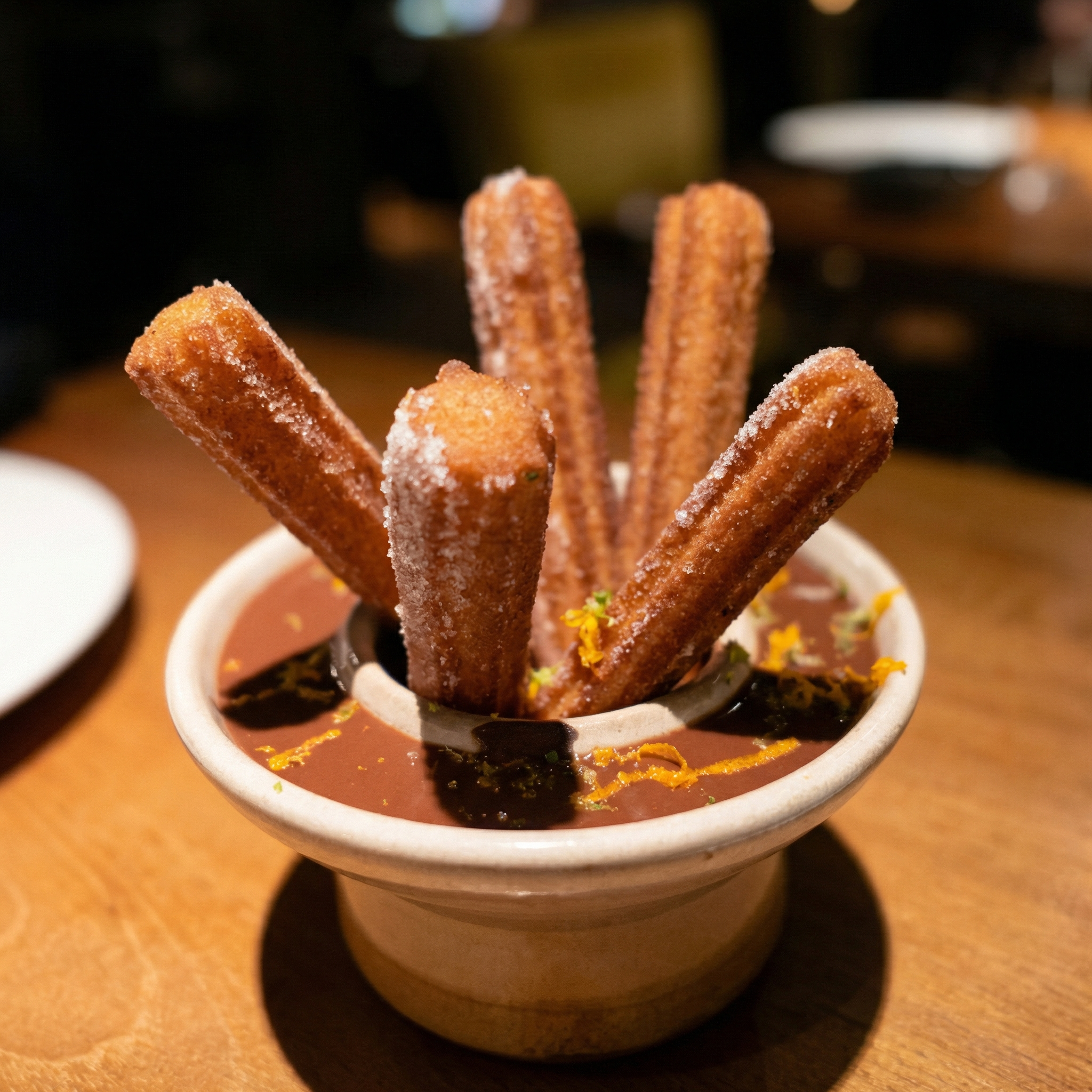 Churros served with chocolate dipping sauce in a small bowl, garnished with orange zest.
