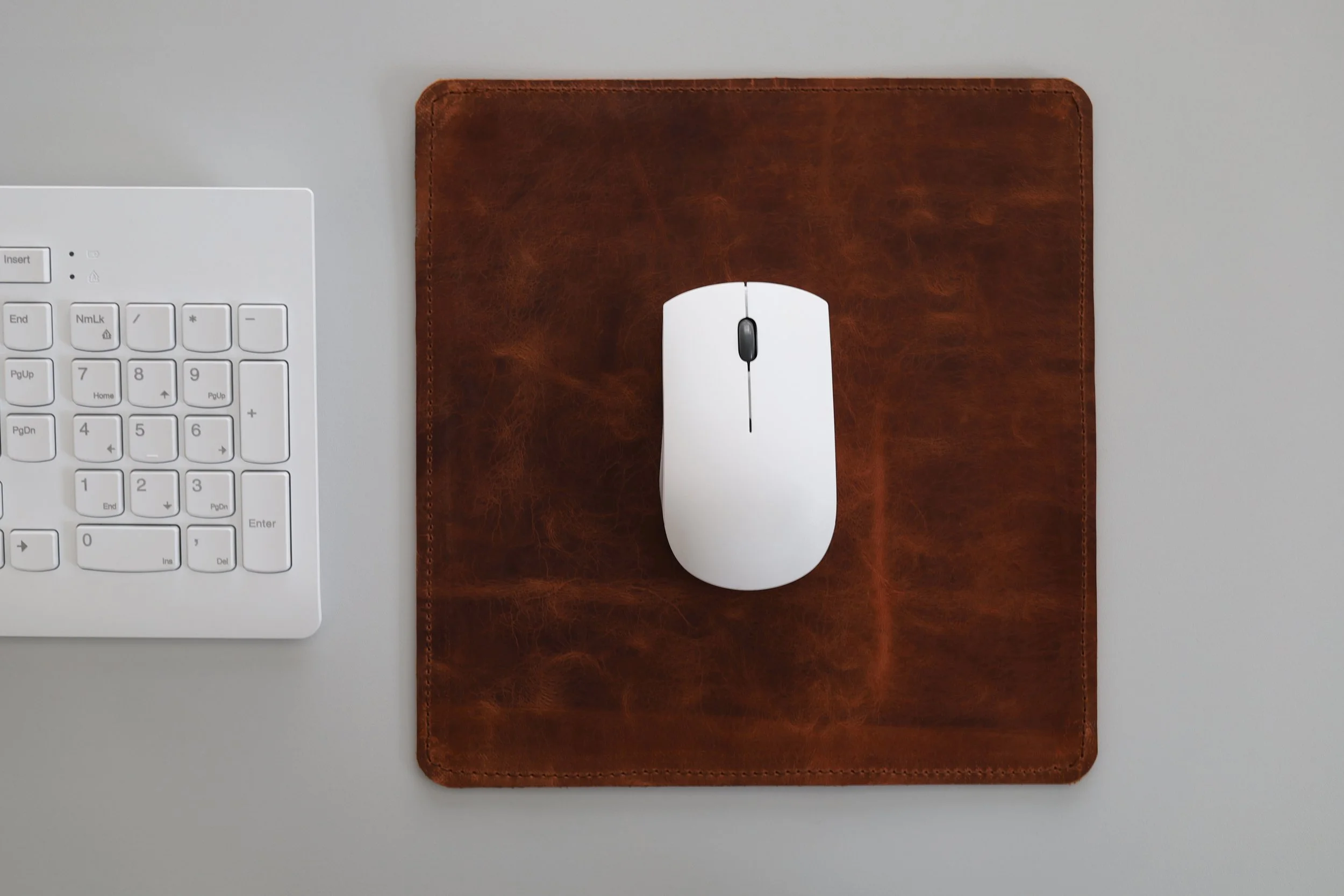 Computer mouse on a leather mouse pad, with a white keyboard partially visible on a gray desk.
