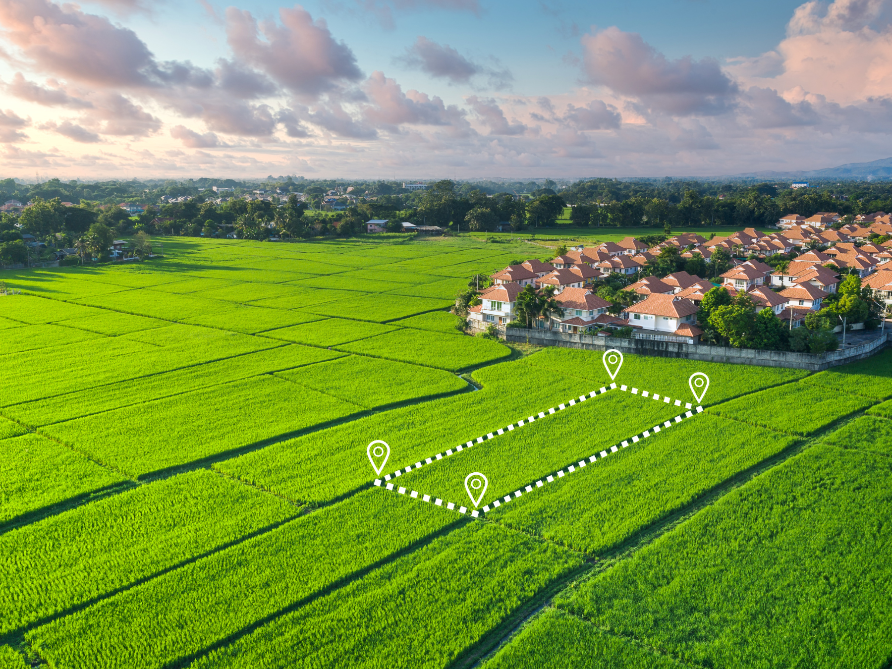Aerial view of green farmland with a residential neighborhood in the background. Overlaid dotted line and four location markers indicating a specific plot of land.