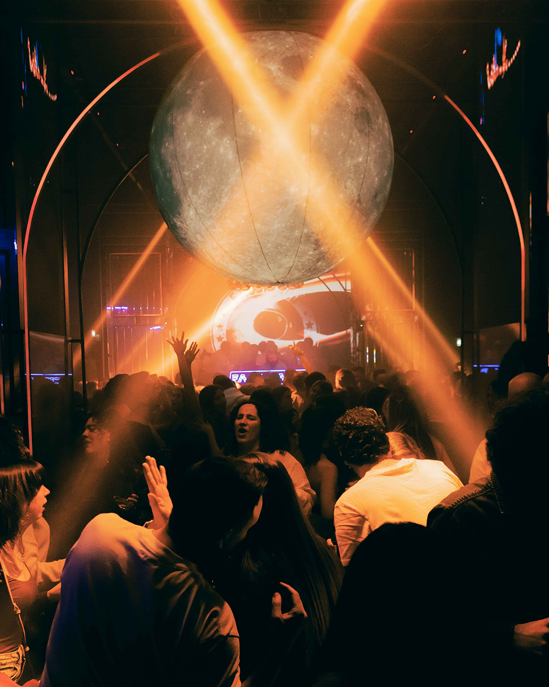 Una multitud en una discoteca con un gran globo que parece la luna y luces de colores brillantes.
