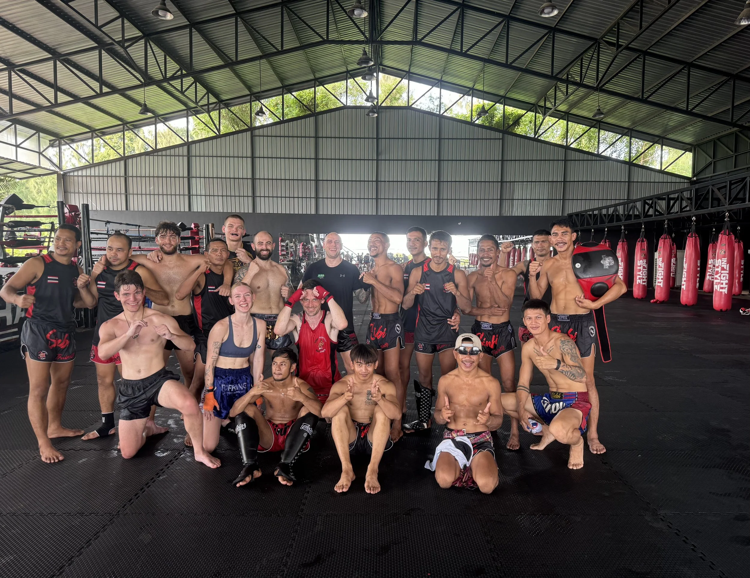 Group of mixed martial artists in martial arts training gear inside a gym, posing for a photo with some making faces and others smiling.