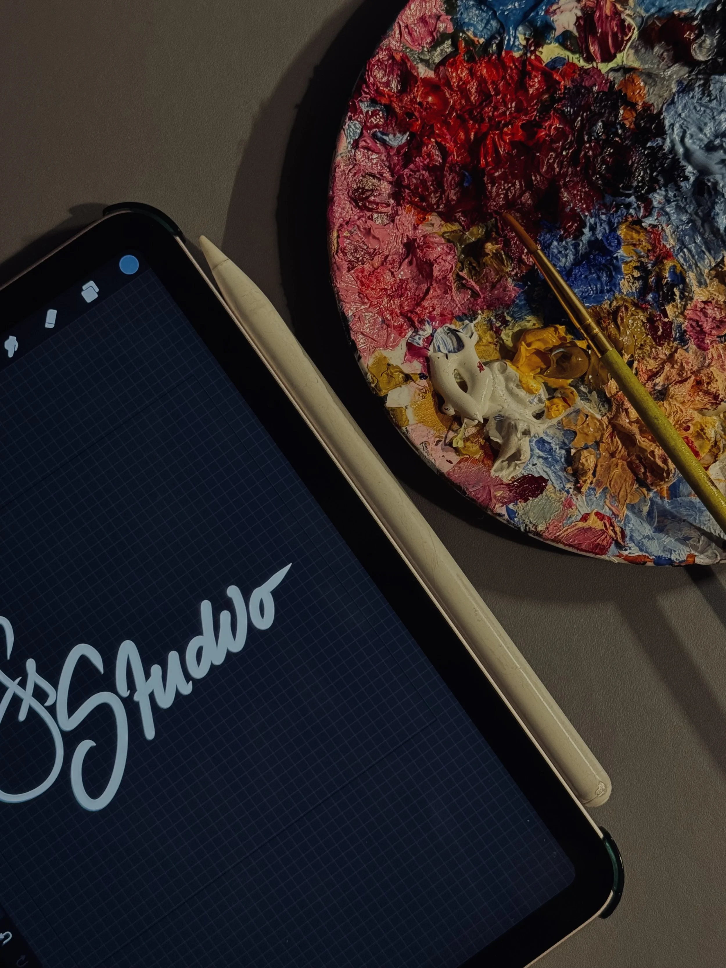 A iPad displaying the word 'Studio' in white cursive font, a colourful paint palette with mixed paints.